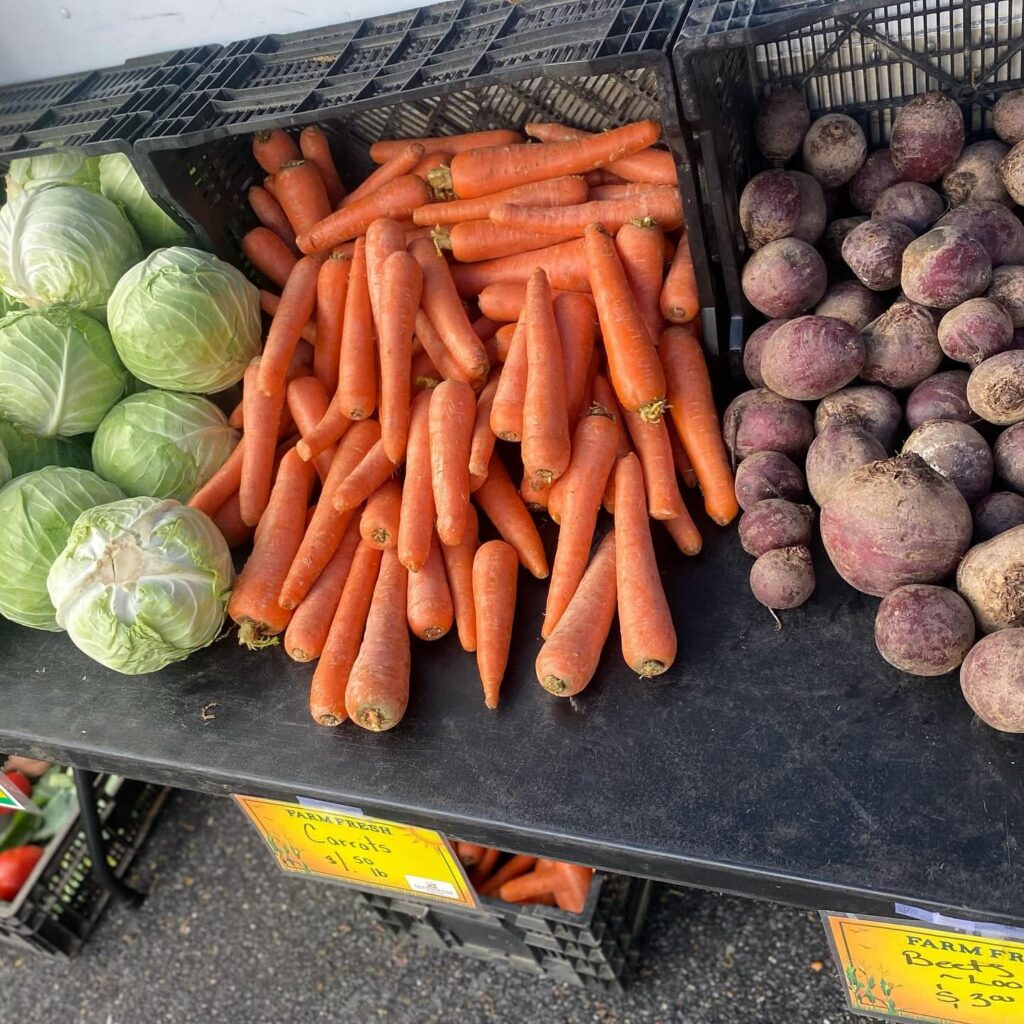 cabbage, carrots, and potatoes on display on a black table at a market